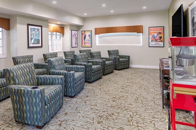 A modern theater room with multiple armchairs in rows, featuring a carpeted floor and artwork on the walls.