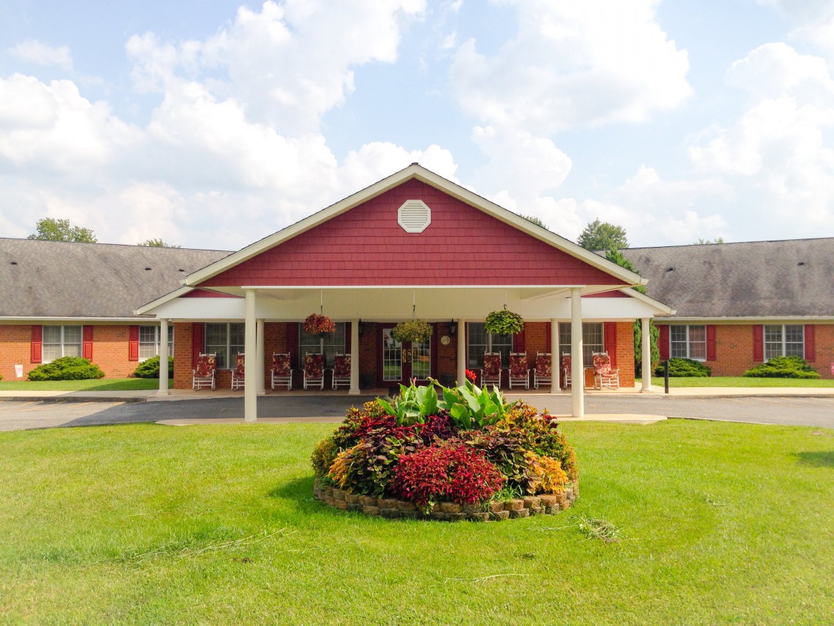 A red building with a covered entrance and landscaped garden in front under a partly cloudy sky.