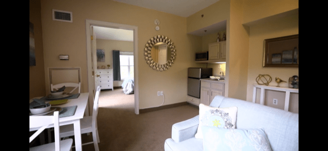 A cozy apartment interior featuring a living area with a small kitchenette and decorative mirror.