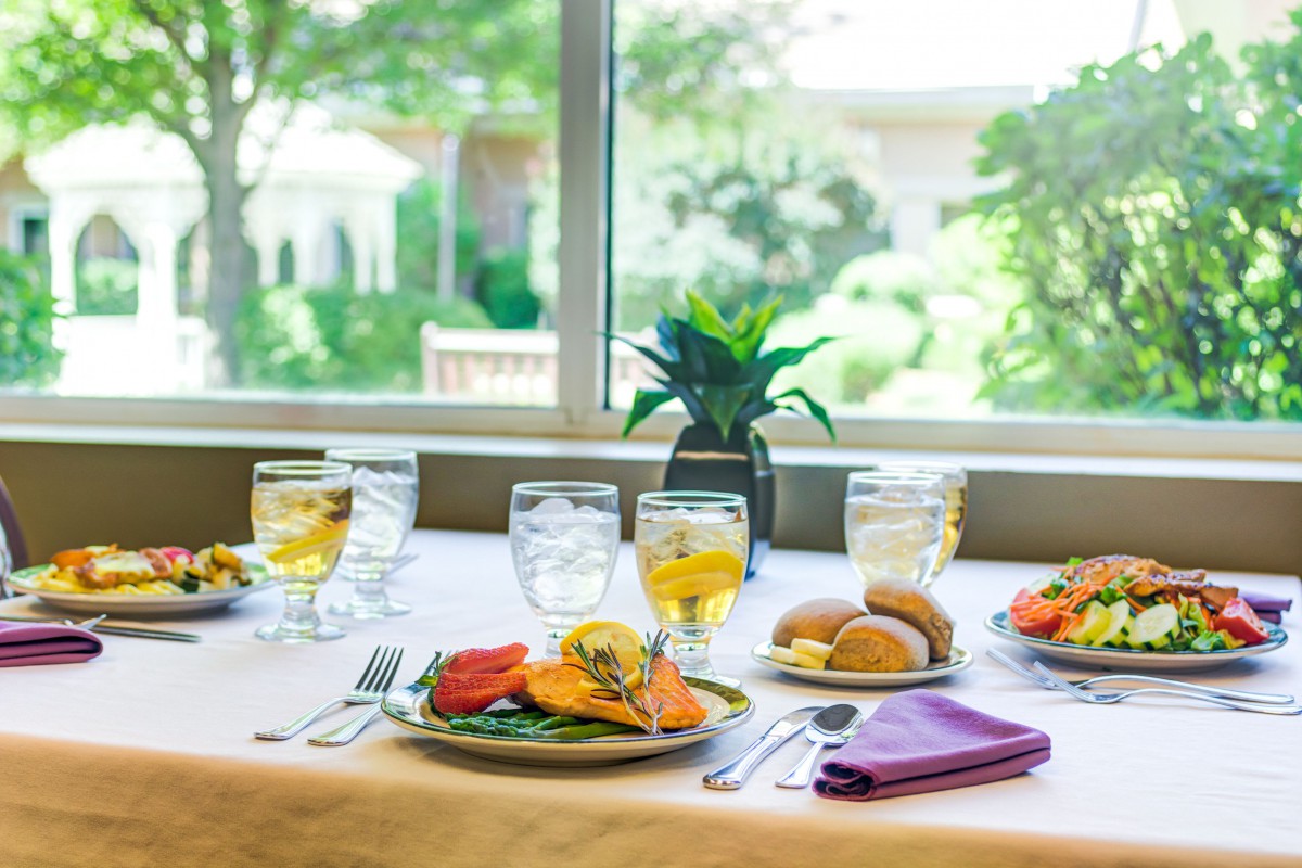 A beautifully set dining table with a meal, glasses of beverage, and elegant tableware.