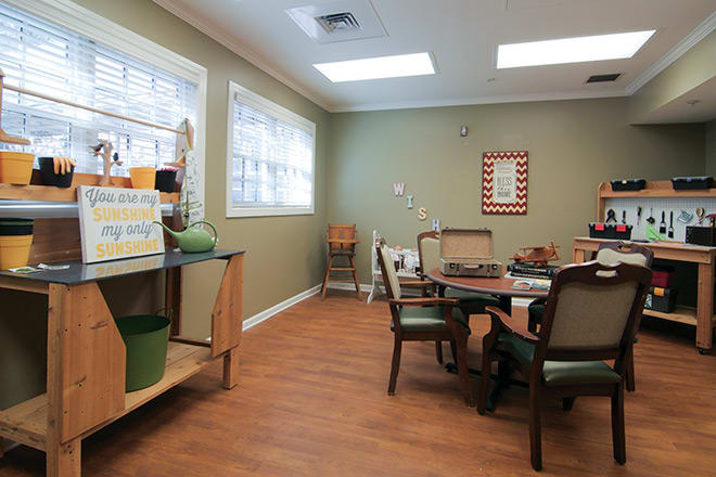 A cozy dining area with tables and chairs, featuring large windows and wooden flooring.
