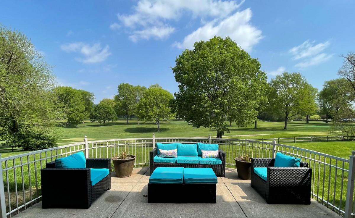 A serene patio setup with turquoise-cushioned furniture overlooking a lush green park and clear blue skies.