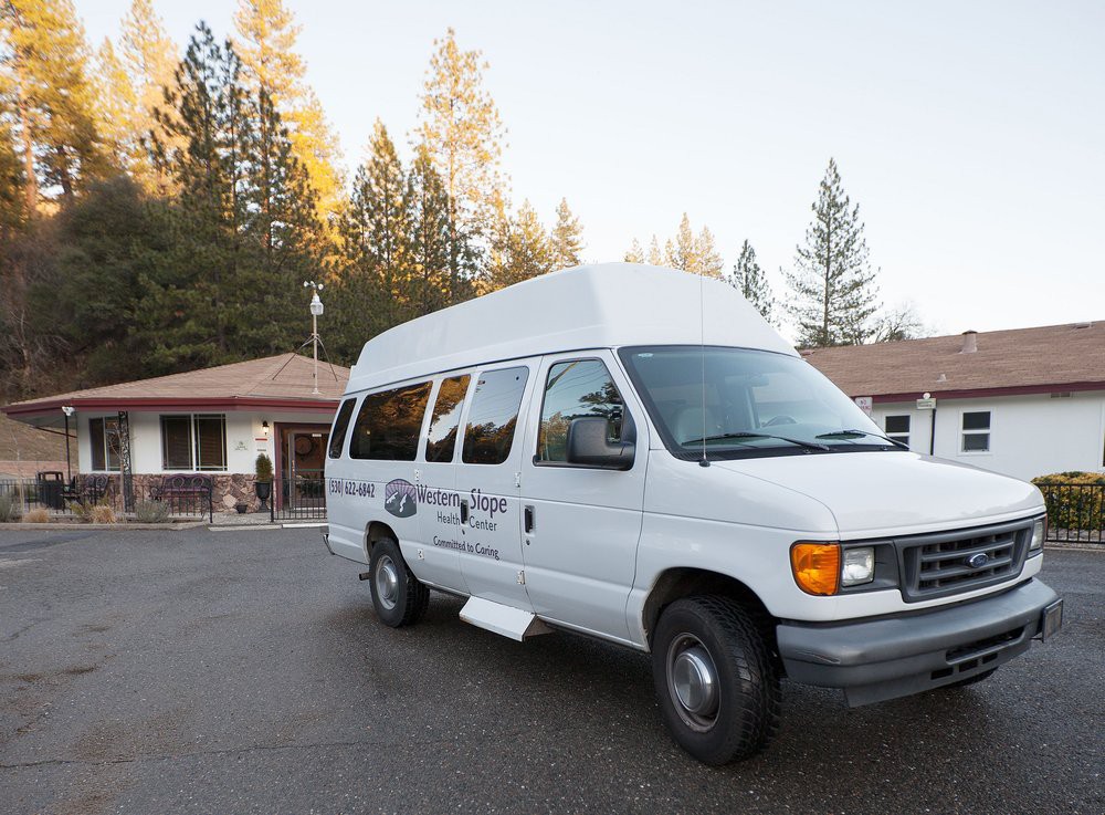 A white van parked in a driveway near a building surrounded by trees.