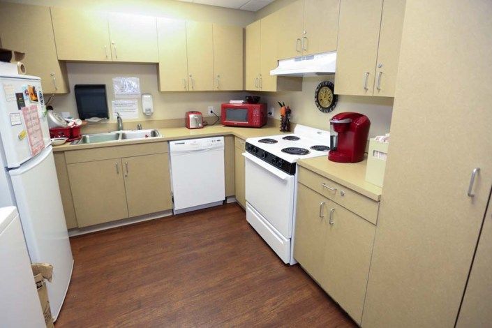 A modern kitchen with wooden cabinets, featuring a stove, microwave, coffee maker, and dishwasher.