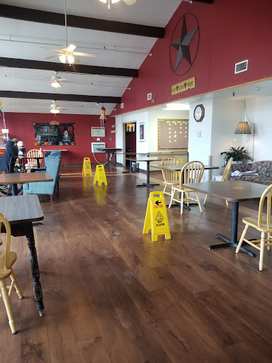 A spacious restaurant interior featuring wooden flooring and caution signs indicating wet floor.
