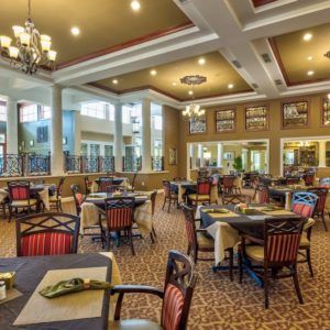 A spacious, elegantly decorated dining hall with neatly arranged tables and chairs under stylish chandeliers.