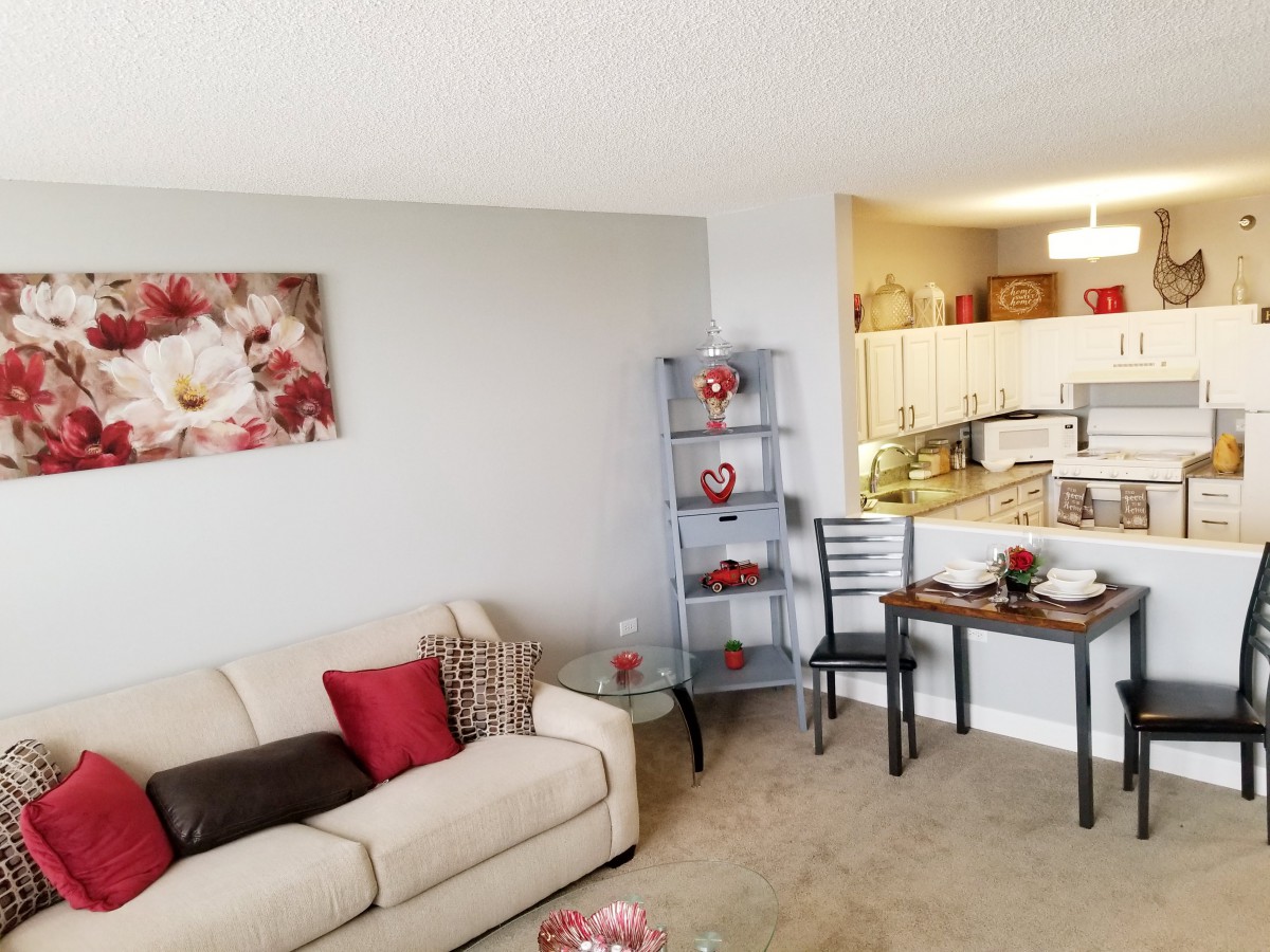 A cozy living room with a sofa, decorative shelves, and a view into the kitchen area.