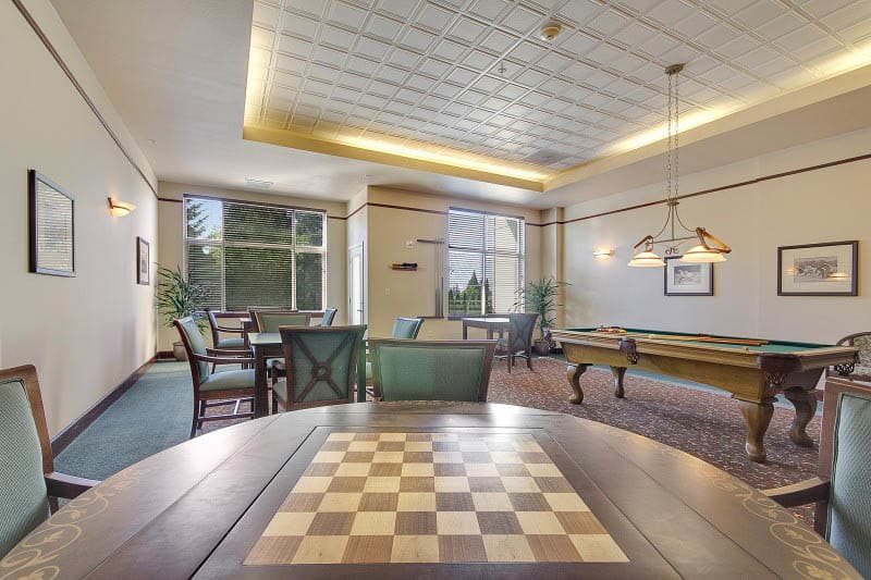A cozy game room with a chess board in the foreground and a billiards table in the background.