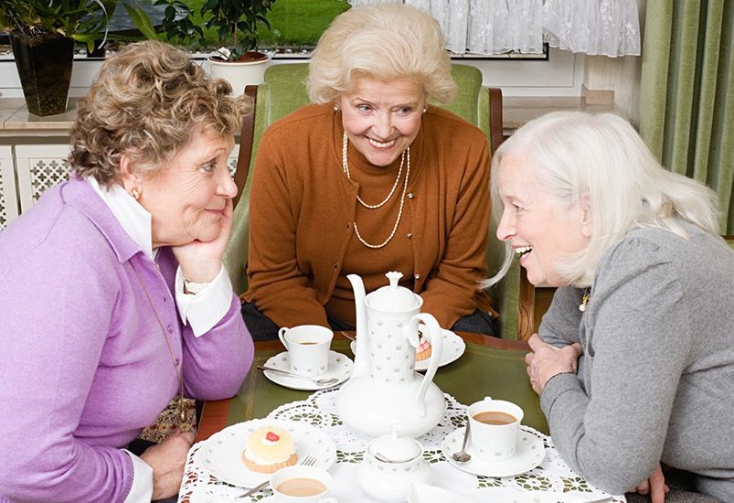 Three elderly women enjoying a tea party and conversation indoors.