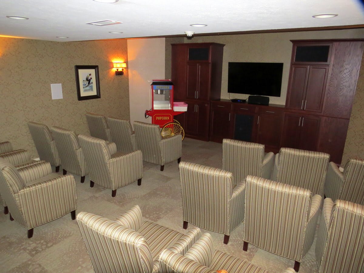 A small theater room featuring several rows of striped chairs, a TV screen at the front, and a popcorn machine.