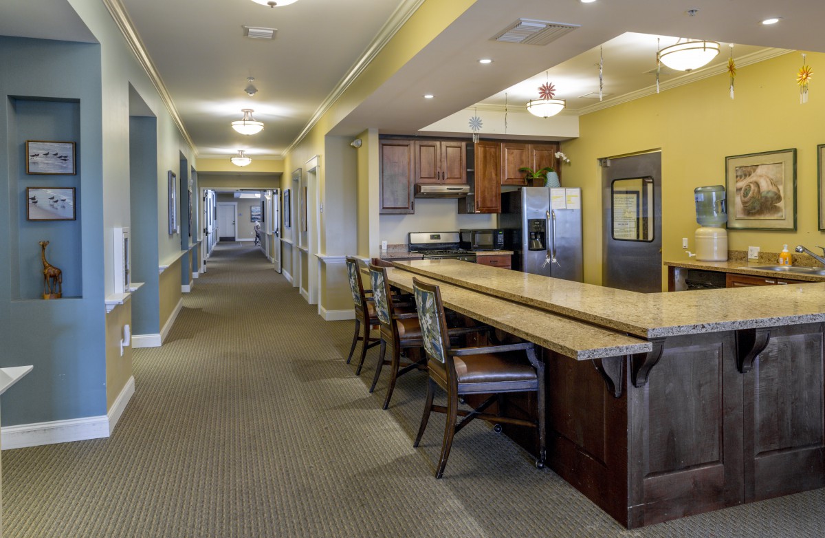 A hallway with a kitchen area featuring wooden cabinets and a countertop with seating.