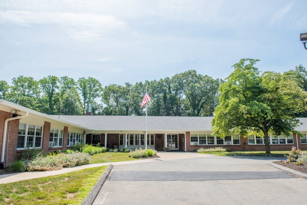 A single-story school building with a driveway and surrounding trees on a clear day.