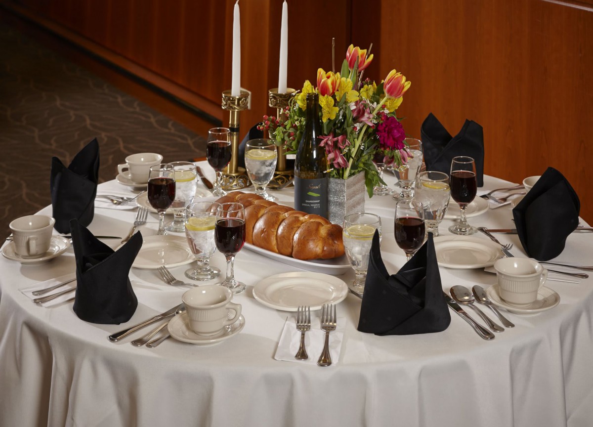 A formal dining table elegantly set with candles, wine glasses, floral centerpiece, and a loaf of bread.