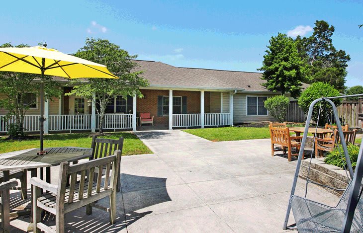 A sunny courtyard with patio furniture and an umbrella in front of a house.