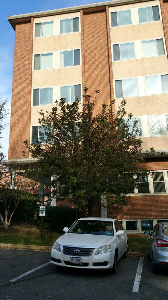 A brick building with several windows, a tree in front, and a parked car.