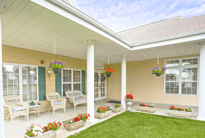 A cozy porch with seating, surrounded by a garden and hanging flower baskets.