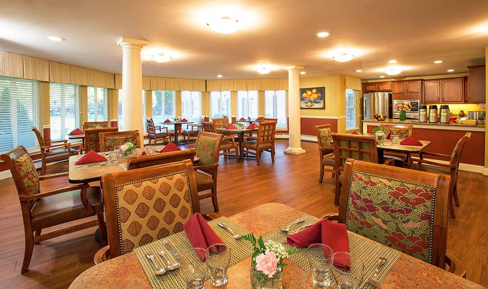 A cozy dining room with elegantly set tables and comfortable chairs, featuring warm lighting and wooden flooring.