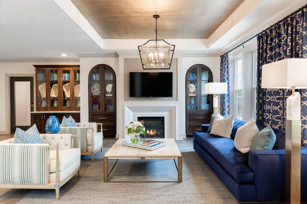 A modern living room featuring a blue sofa, stylish lighting fixture, and a cozy fireplace, flanked by built-in bookshelves.