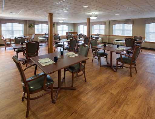 A spacious dining room featuring wooden tables and chairs, illuminated by natural light streaming through large windows.