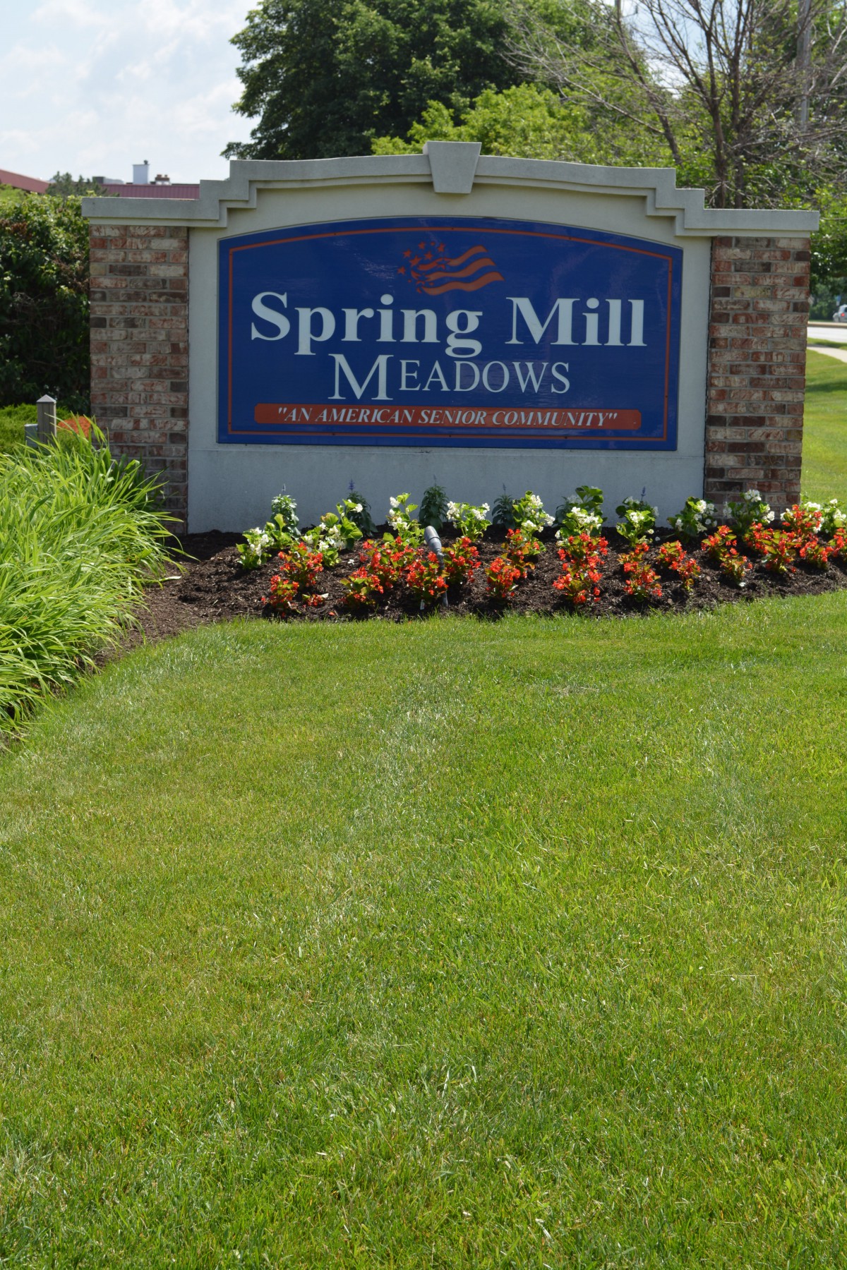 Entrance sign for Spring Mill Meadows surrounded by landscaped flowers and grass.