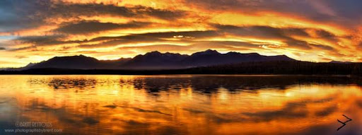 A breathtaking sunset over the mountains, reflecting on calm waters.