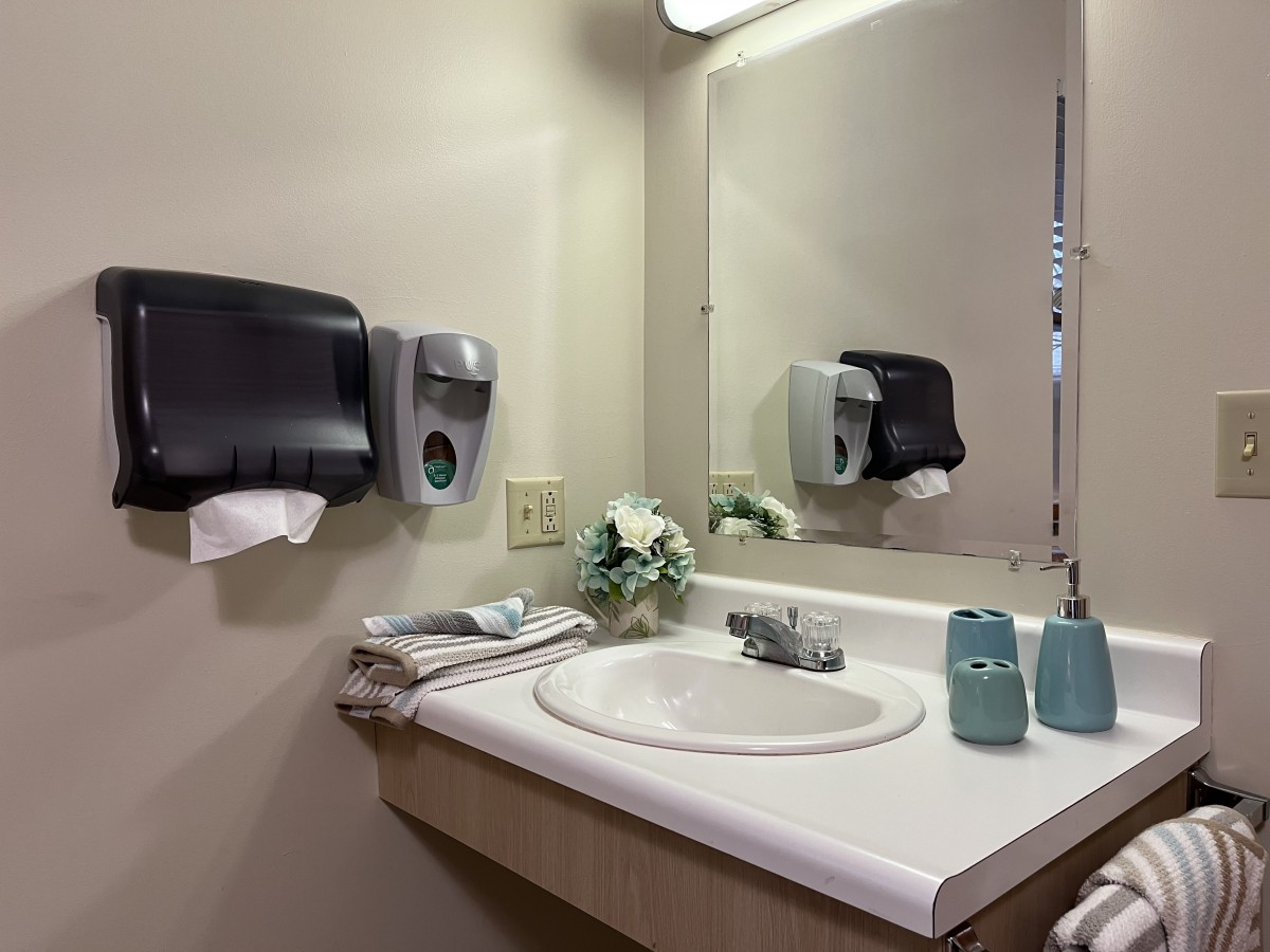 A clean and tidy bathroom with a sink, mirror, and dispensers.
