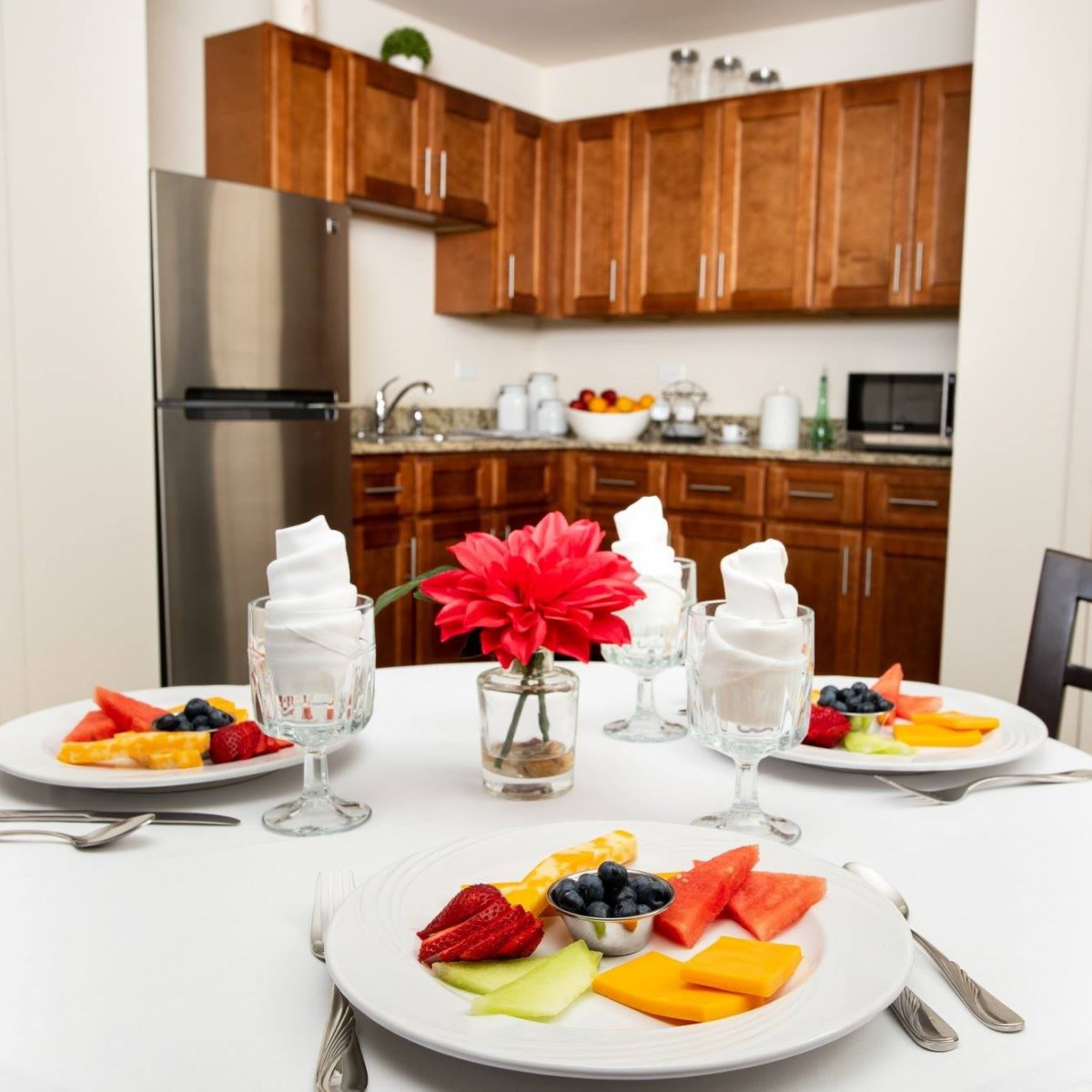 A modern kitchen with a neatly set dining table featuring fresh fruit plates and dessert.