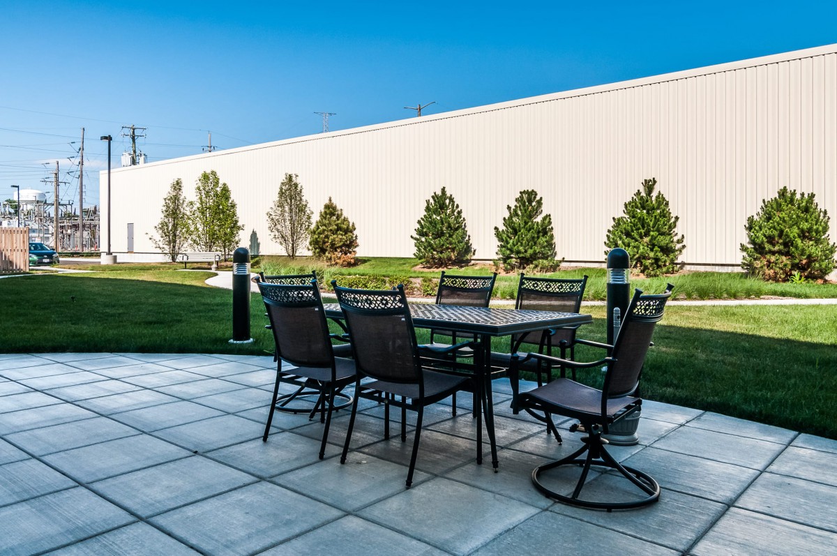An outdoor patio setup with a table and chairs on a paved surface, surrounded by greenery.