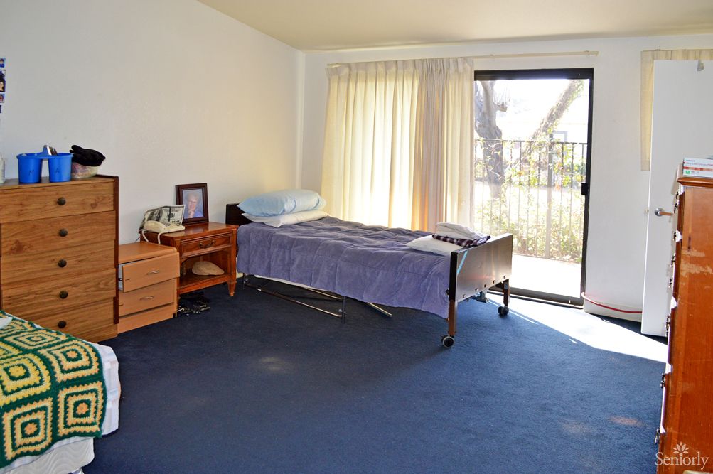 A spacious room with a hospital bed, desk, and large window with curtains.