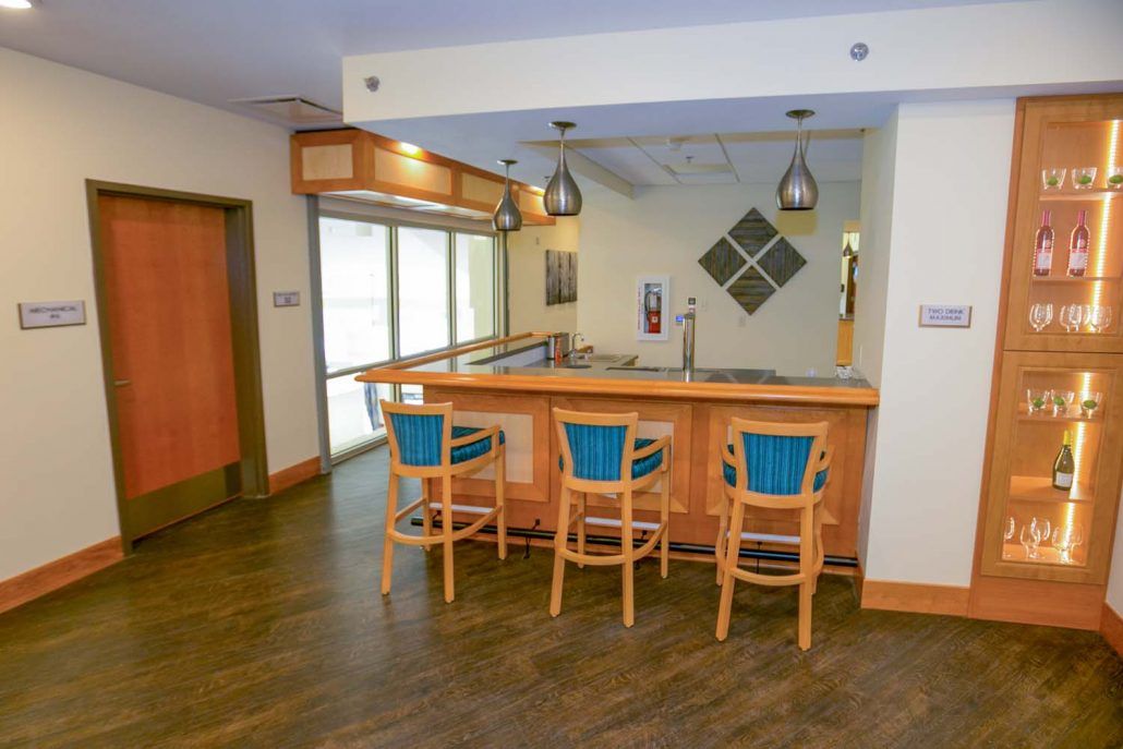 A modern home bar setup with wooden stools and pendant lighting.