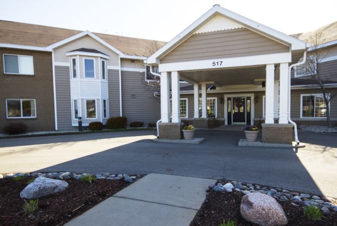 The image shows the front entrance of a hotel with a covered driveway and landscaped surroundings.