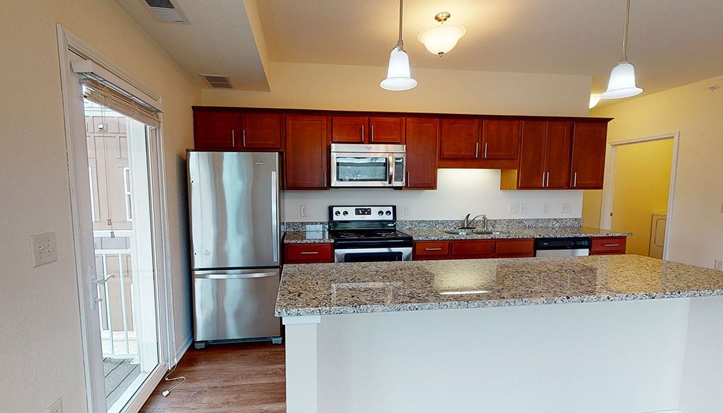 A modern kitchen featuring stainless steel appliances, granite countertops, and wood cabinets.
