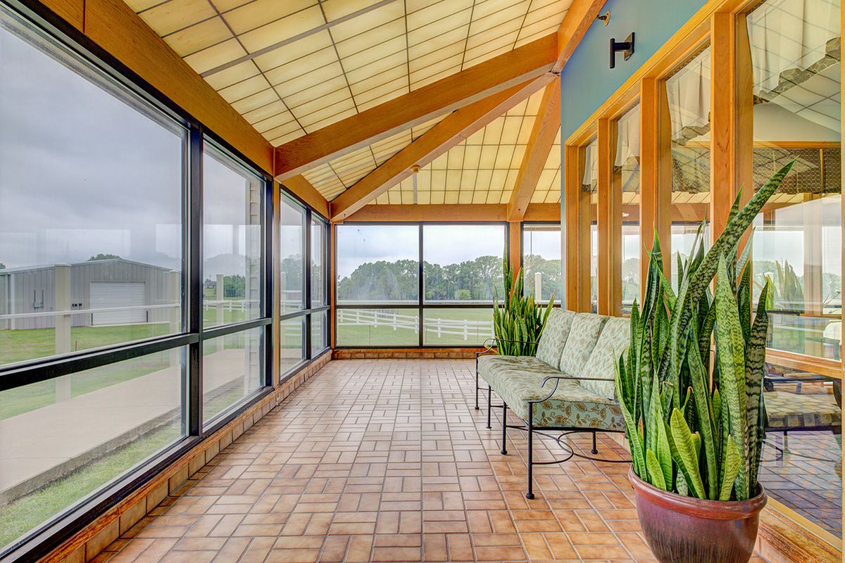 A spacious sunroom with glass windows, tiled flooring, and comfortable seating adorned with potted plants.