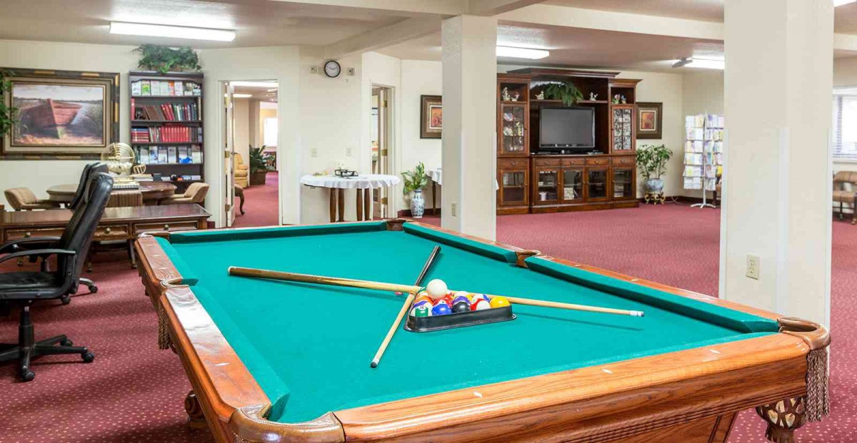 A recreation room featuring a pool table with cue sticks and balls, and a TV in the background.
