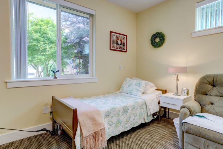 A cozy bedroom with a single bed next to a window, featuring a bedside lamp and table.