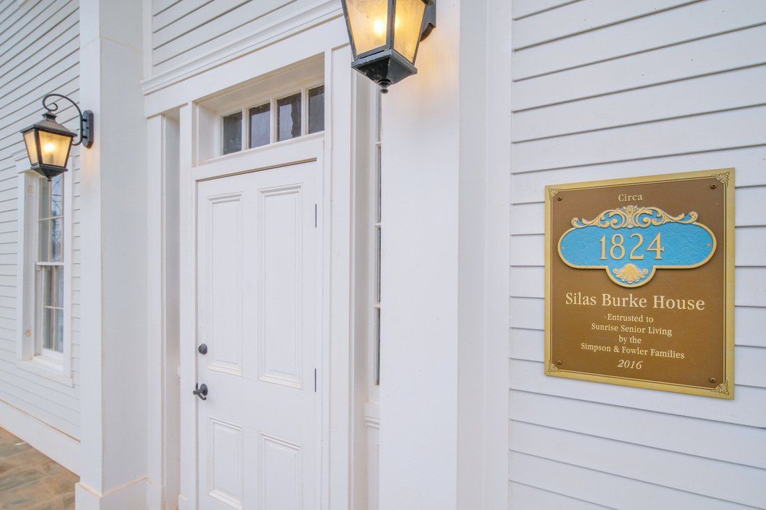 A white exterior with a door and plaque next to a lamp.