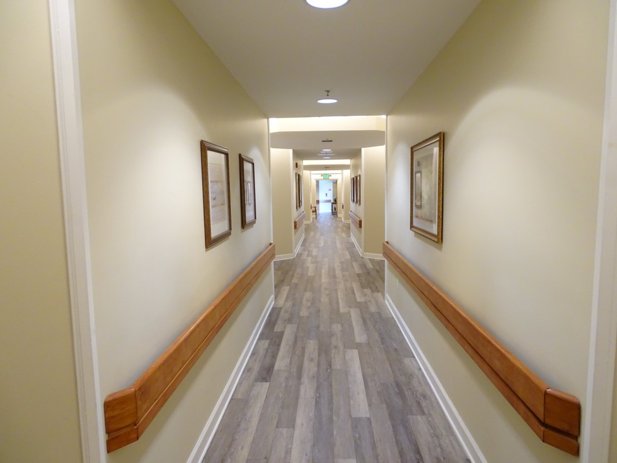 A well-lit hallway with wooden flooring and handrails, adorned with framed artwork.