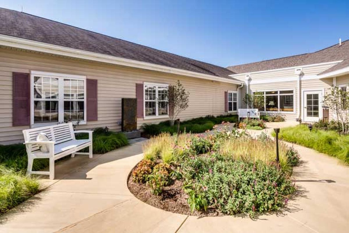A peaceful exterior view of a building with well-maintained landscaping and benches along a curved pathway.