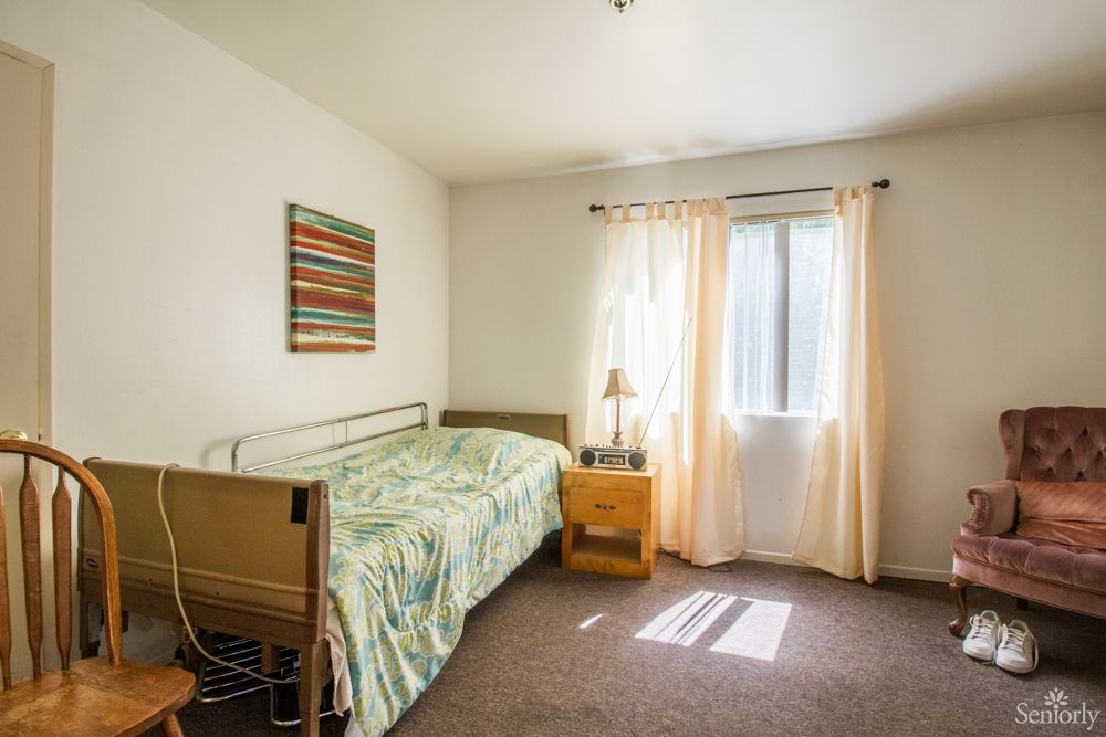 A simple bedroom with a hospital bed and natural sunlight streaming through the window.