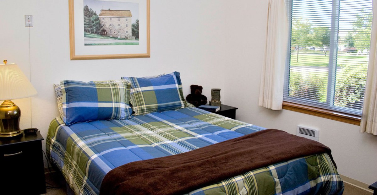 A cozy bedroom with a plaid-patterned bed and framed artwork on the wall.