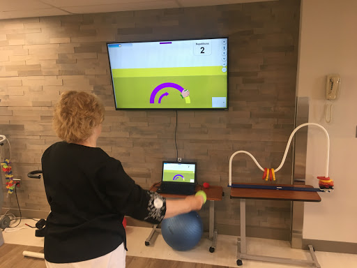 A person engages in a rehabilitative exercise using an interactive gaming system set up alongside a large screen.