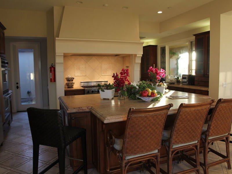 A cozy kitchen with a large island and stylish chairs, adorned with flowers and fresh fruit.