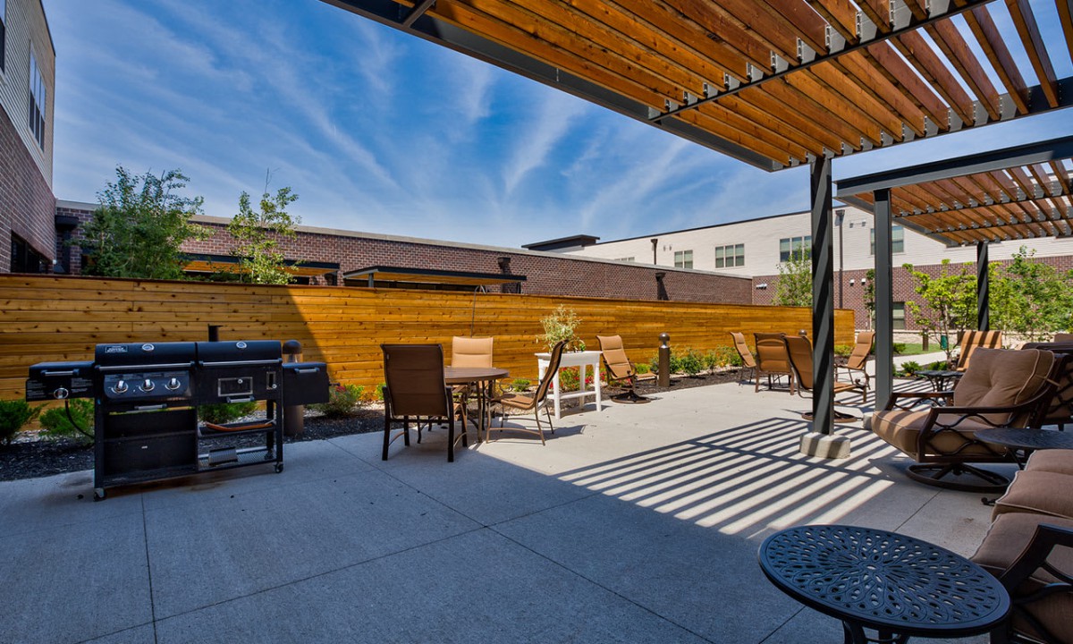 An outdoor patio with seating, a pergola providing shade, and a barbecue grill on a sunny day.
