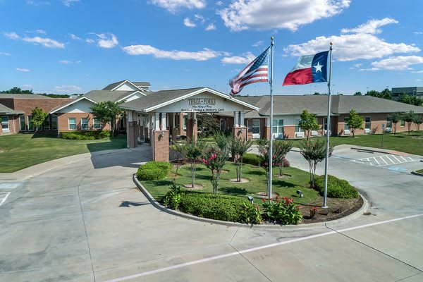 An entrance to a residential building with an American and Texas flag, surrounded by greenery.