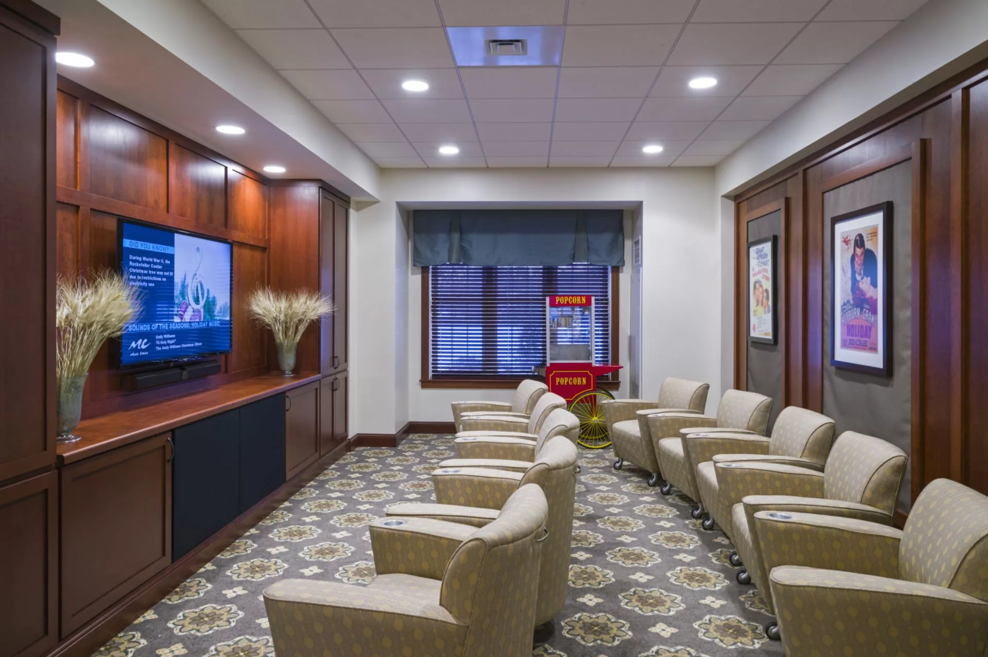 A well-furnished waiting room with rows of chairs facing a television, featuring elegant decor and indoor lighting.
