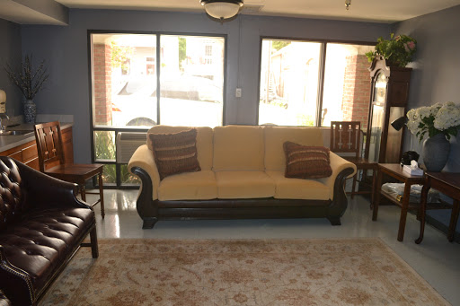 A cozy living room featuring a beige sofa, wooden chairs, and ample natural light.