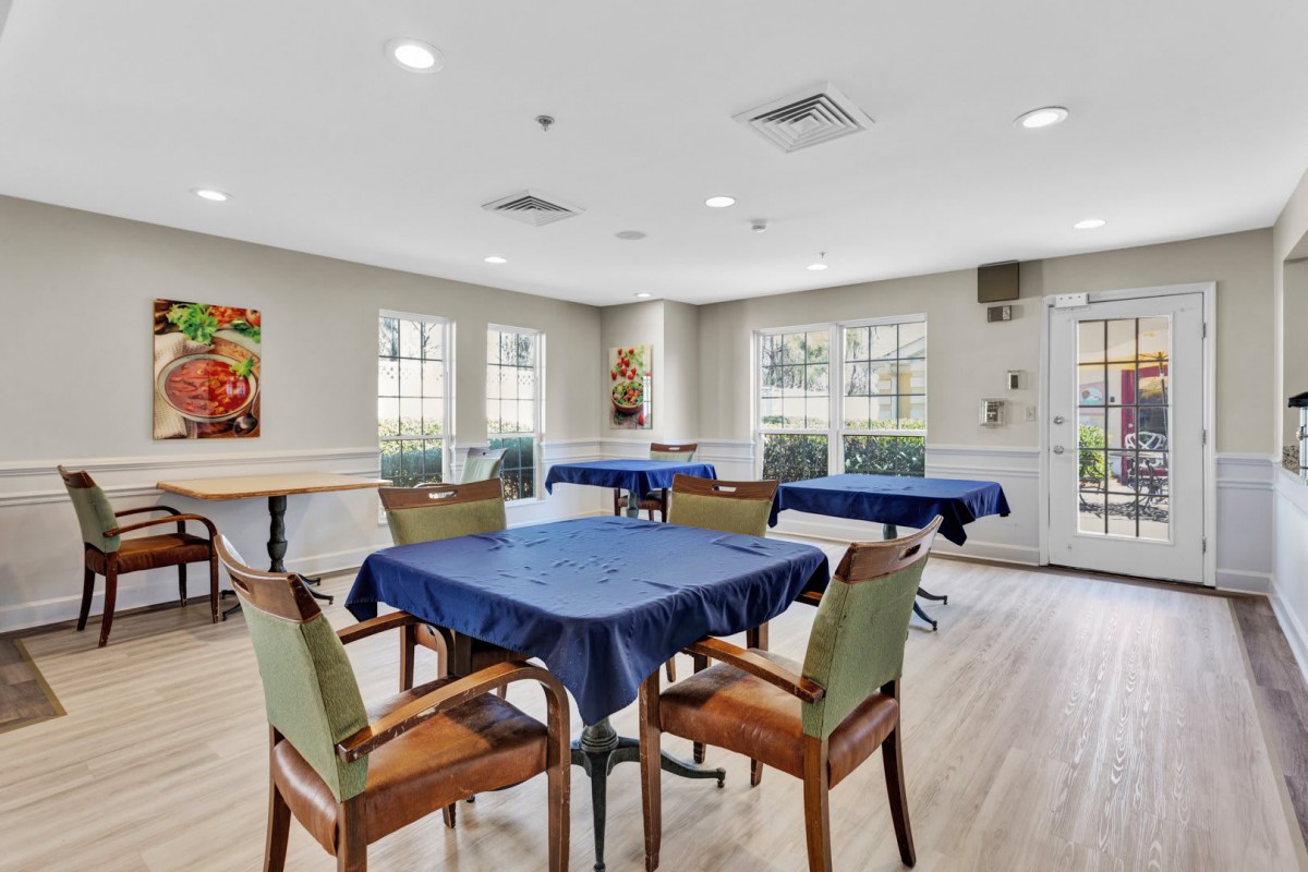 A well-lit room with tables and chairs, featuring blue tablecloths and a wooden floor.