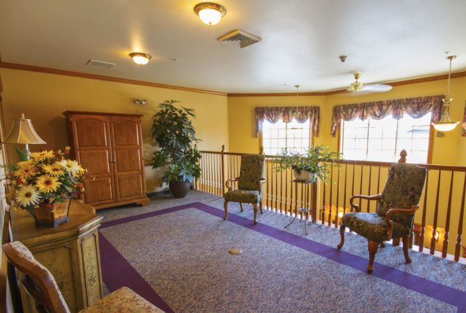 A cozy living room area with chairs, a large wooden cabinet, and indoor plants in a well-lit space.