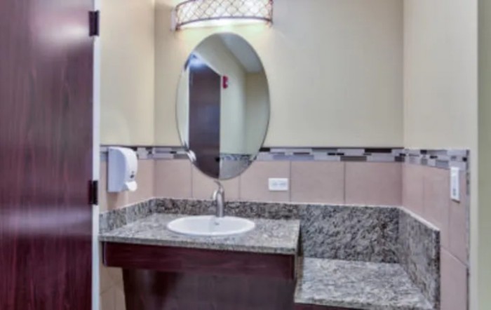 A modern bathroom with a granite countertop and an oval mirror.