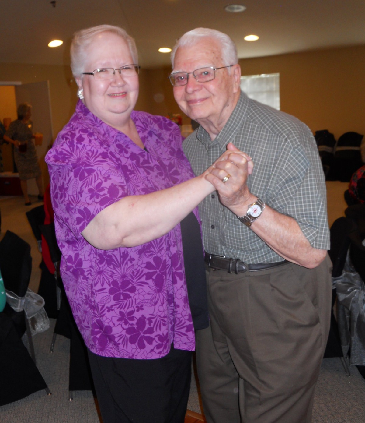 An elderly couple happily dancing together indoors.